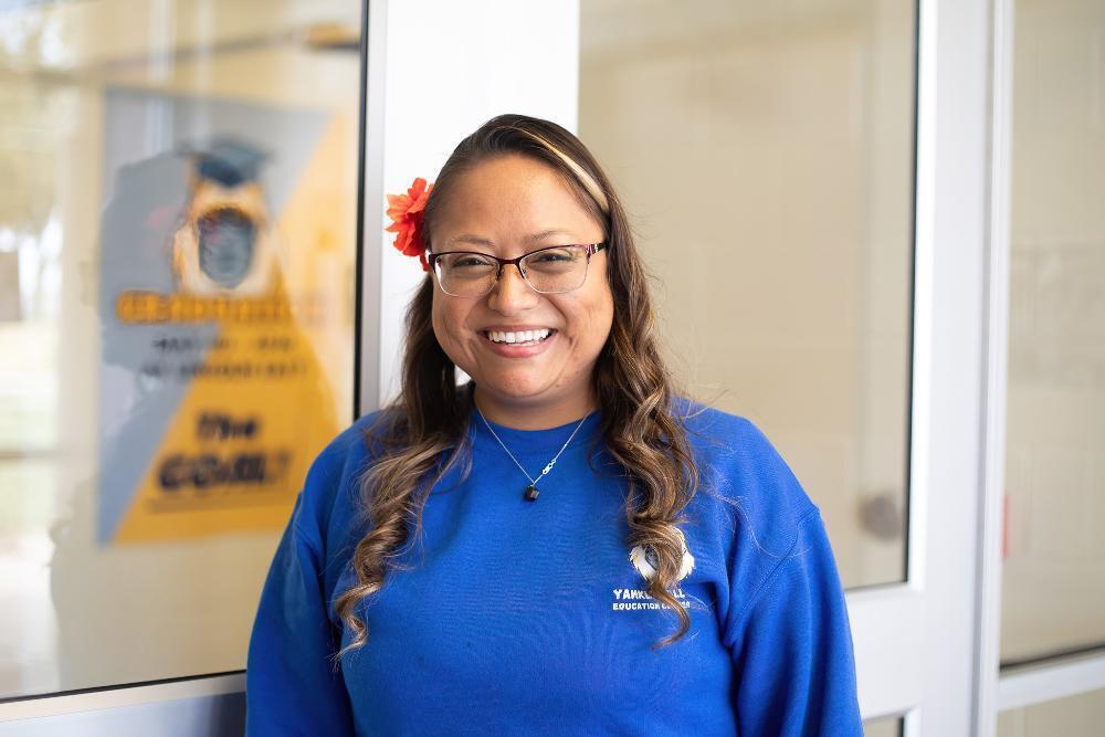 A woman smiles, wearing a blue sweatshirt that says "Yankton Education Center," near a glass door.