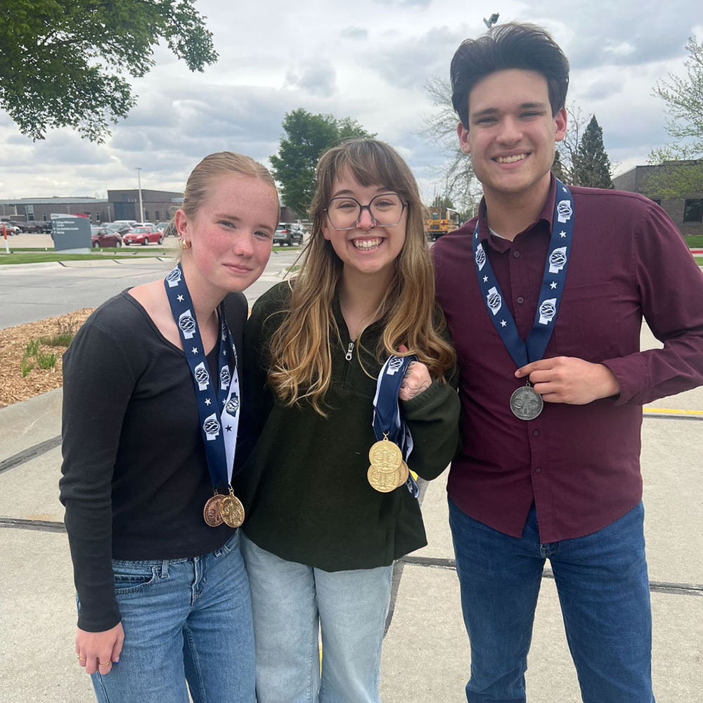Lincoln Southwest journalism advisor Delani Young stands in between Southwest journalism students Addison and Joshua. Addison and Joshua are both wearing state medals, and Delani is holding medals from the team's trip to the NSAA State Journalism Championships.