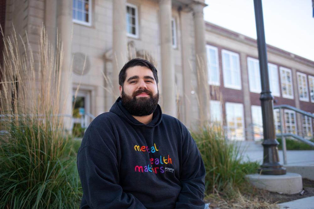 A man sitting in a classroom wearing a black sweatshirt.