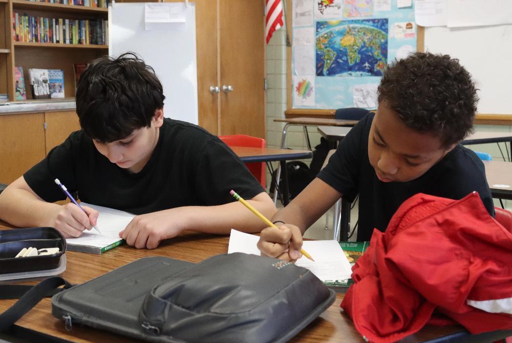 From left, Lefler students Aryos and A'mare use pencils in their right hands to complete a writing assignment at their desk. They are filling out a worksheet on top of a workbook.