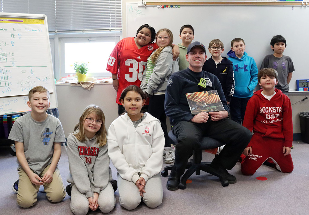 A Lincoln firefighter is surrounded by ten Huntington Elementary School students. The firefighter is holding a book he has been reading to them.