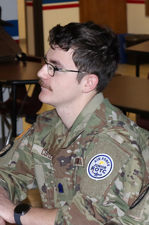 AFJROTC member Colin sits at a desk in the focus program classroom. He is listening to a presentation at the front of the classroom.