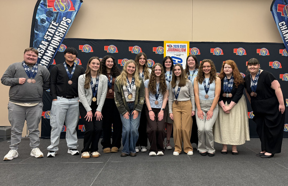 Thirteen Southeast students stand in two rows at the NSAA State Journalism Championships. They are all wearing medals around their necks after winning state awards.