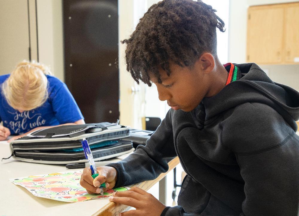 A student at Moore Middle School works on an art project at a table in his classroom, using a paint brush to apply color.