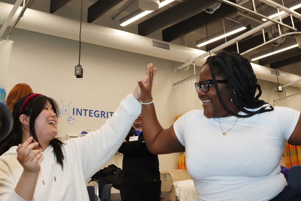 Two Bryan College of Health Sciences Focus Program students share a high five after completing a CPR activity in her classroom. Both girls are smiling and are looking at each other.