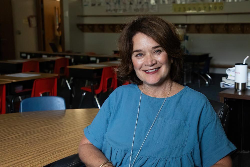 A woman sitting in a classroom, wearing a blue shirt.