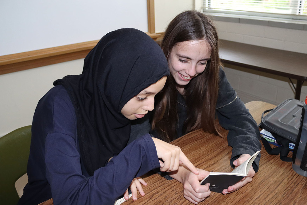 Two Culler Middle School eighth graders smile as they read a pocket-sized copy of the United States Constitution. One girl is holding the book and a second girl is pointing at words at the righthand side of one of the pages.