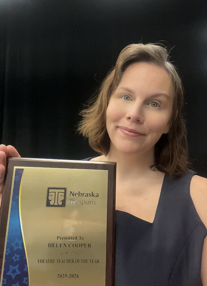East teacher Helen Cooper stands in the school auditorium with her plaque for winning the 2025-26 Nebraska Thespians Theater Teacher of the Year Award. She is the school's theater director.