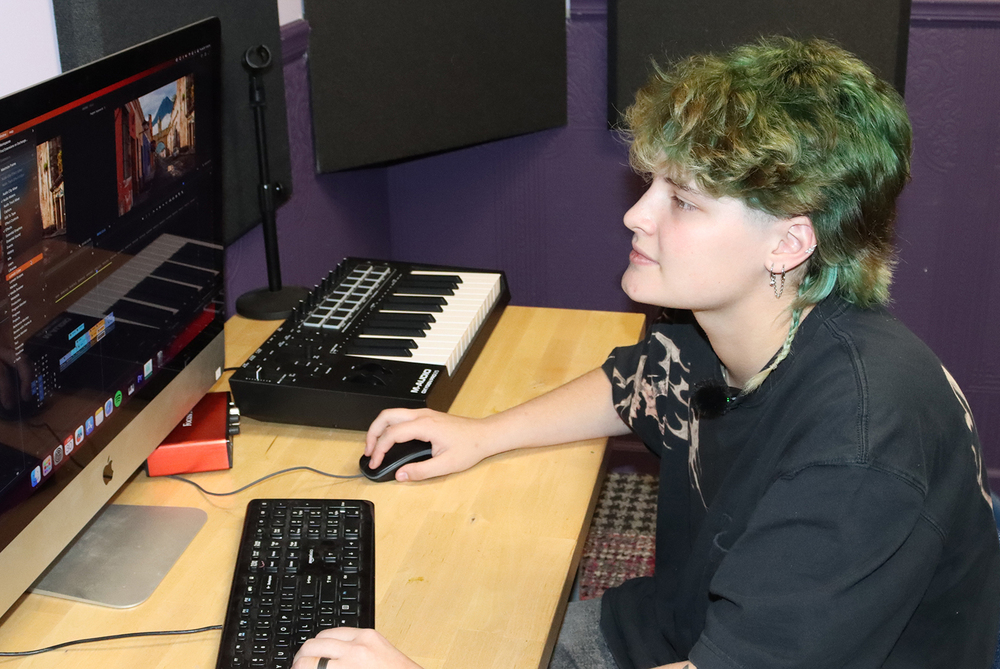 Bay High Focus Program senior Lexie works on a computer program in a Bay High Focus Program studio room. She is holding a mouse with her right hand and is typing on a keyboard with her left hand.