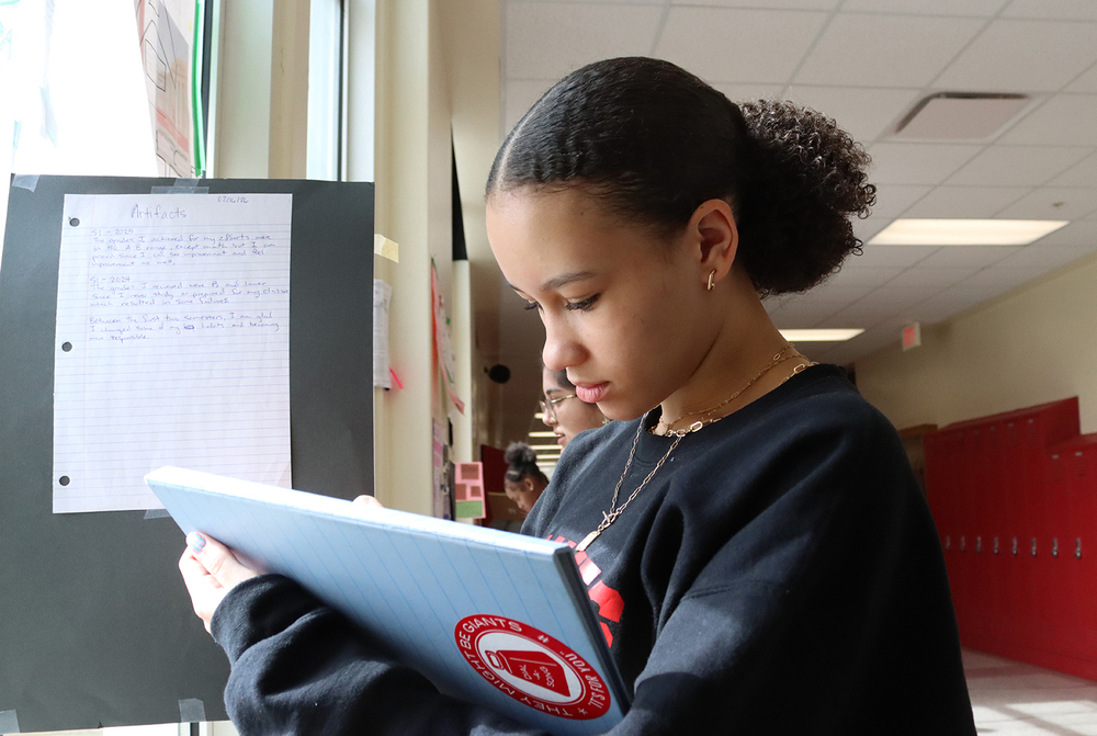 Lincoln High junior Josephine writes down comments as she looks at part of a poster that is hanging in a hallway.