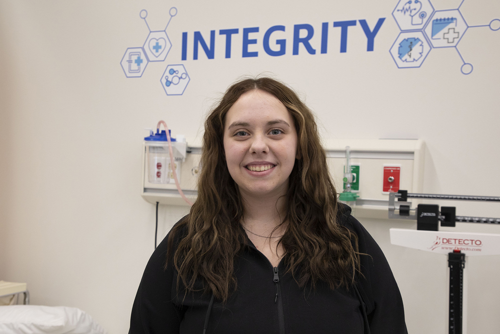 Bryan College of Health Sciences Focus Program student Sydney smiles in a classroom. The word Integrity is on a wall behind her.