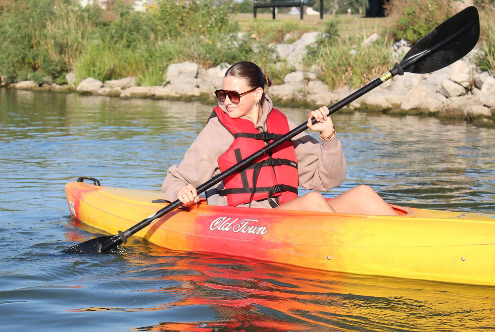 A Southwest High School student is paddling in a kayak at Holmes Lake. She is holding her paddle with both hands and is dipping one of the paddles in the water.