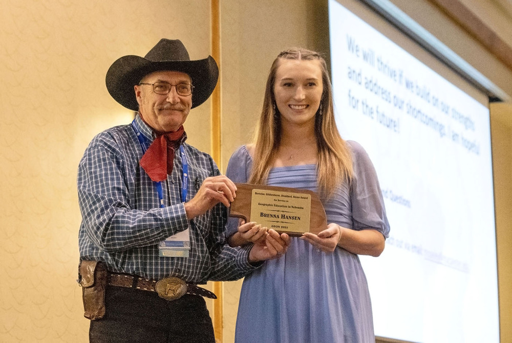 Lincoln High social studies teacher Brenna Hansen smiles with a state award on a stage. She is standing next to a man who is presenting the award to her.
