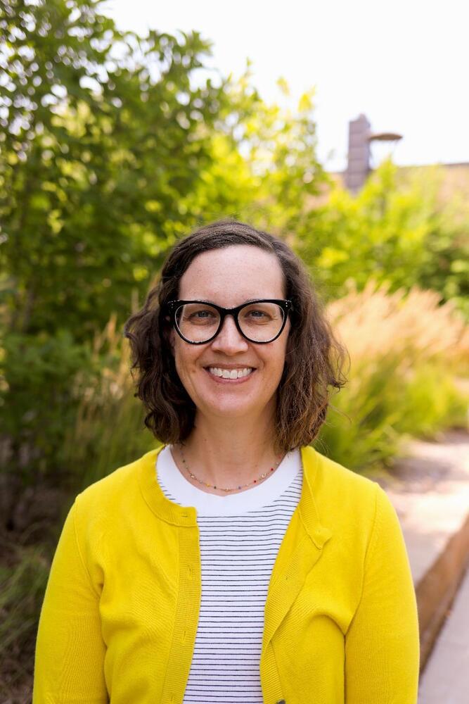 A woman standing outside wearing a yellow sweater.