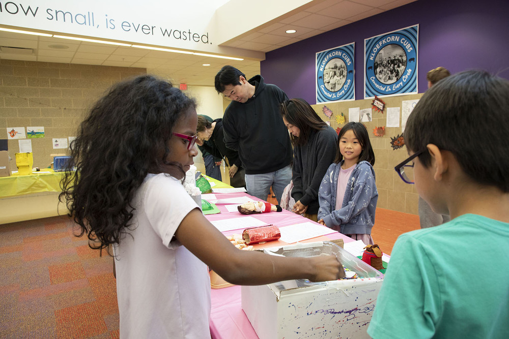 Two Kloefkorn Elementary students interact  with a piece of artwork on a display table as families observe other art.