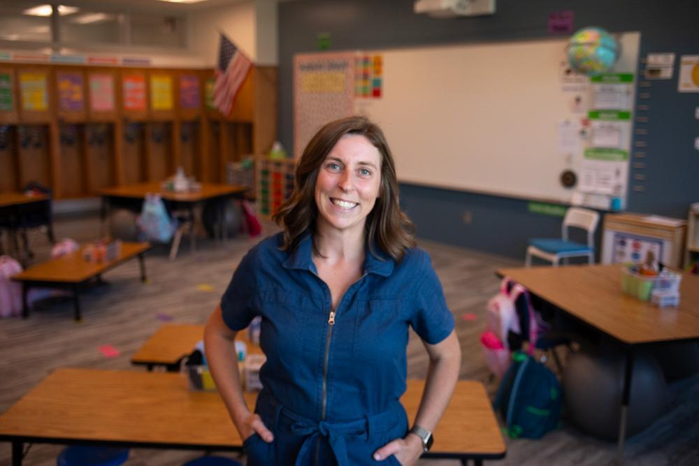 A woman standing in a classroom wearing a blue jumpsuit.
