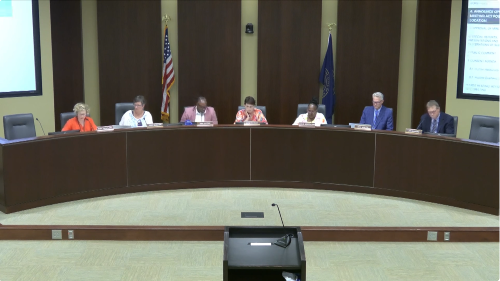 Five members of the Board of Education sitting at the front of the boardroom with Superintendent John Skretta and legal counsel Jim Gessford.
