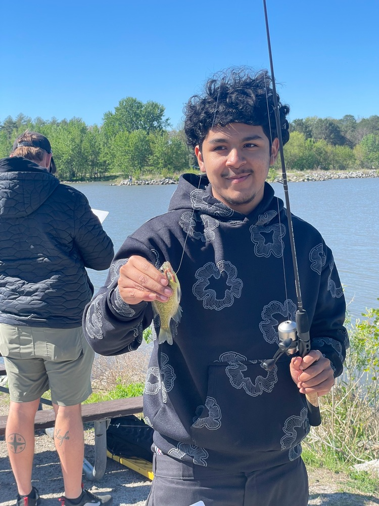a young man holds a fish he caught, and smiles