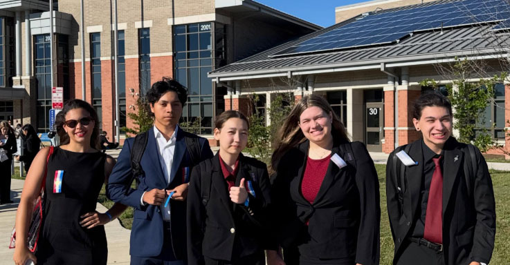 From left, Sophia Allen, Braxton Wiebke, Jubilee Lathrop, Emersyn Smith and Alfredo Ramirez smile at the National Speech and Debate Tournament. The Northwest and Southeast students are standing in a row in front of a large high school that is the site of their contests. The high school is several stories tall and has brick columns on the front wall.