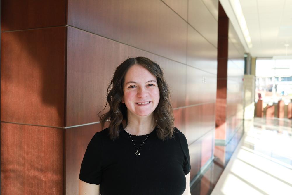 A woman standing inside a building hallway wearing a black shirt.