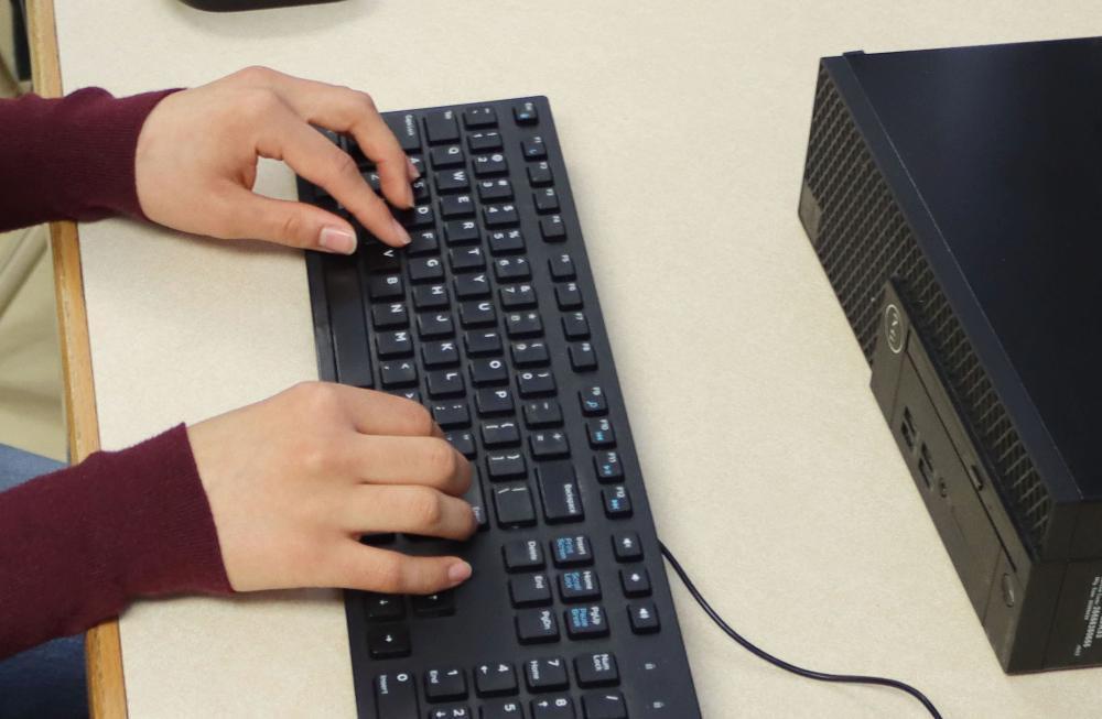 Two hands of a student are typing on a keyboard in a classroom at Southeast High School, taking part in the AP Capstone program.