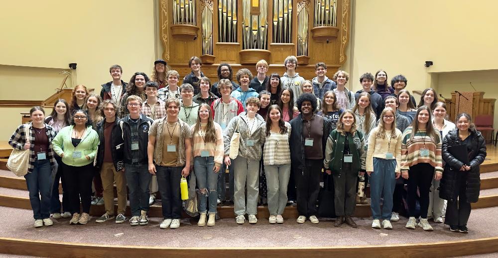 Four rows of Lincoln Public Schools students smile on a stage with a pipe organ in the background. There are more than 40 high school students in the picture. All of them sang in the Nebraska Music Educators Association All-State Choir.