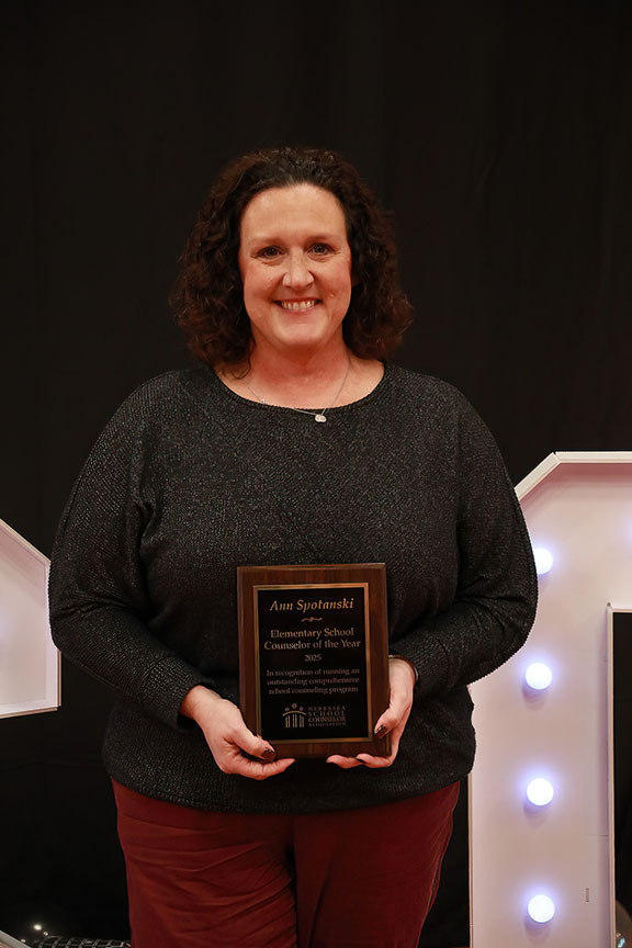 Ann Spotanski smiles while holding her state award plaque in front of her with both hands. She is a school counselor at Clinton Elementary School.