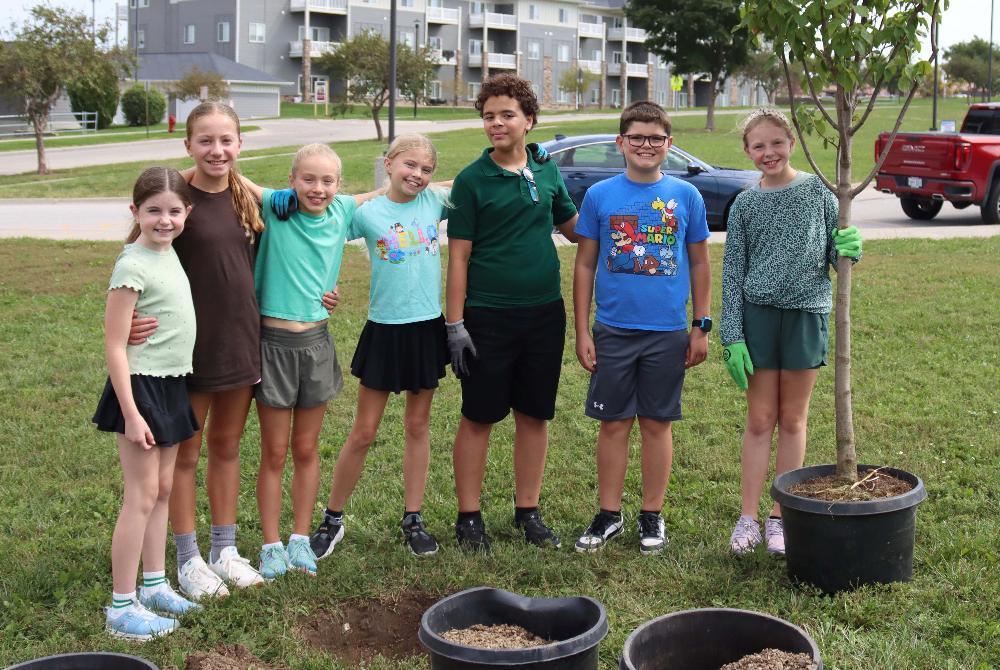From left, Adams Elementary School students Penny, Linden, Keira, Harper, Mason, Oliver and Lulu smile after planting trees near their school.
