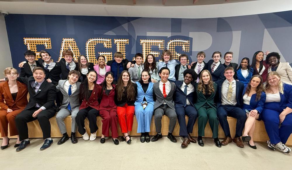 A large group of young adults, mostly in suits, sits together smiling for a photo.
