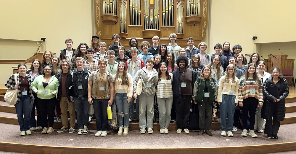 More than three dozen LPS high school choir students stand on a stage in front of an organ.
