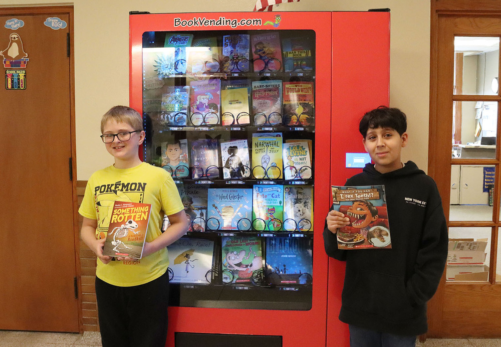 Two students hold books they have chosen from a book vending machine. The machine has five rows of books that Saratoga Elementary School students can pick as a reward for doing well in class.