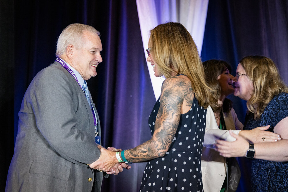Lincoln East High School Club advisor Sarah Staples-Farmer international recognition at convention on stage shaking hands with a man.