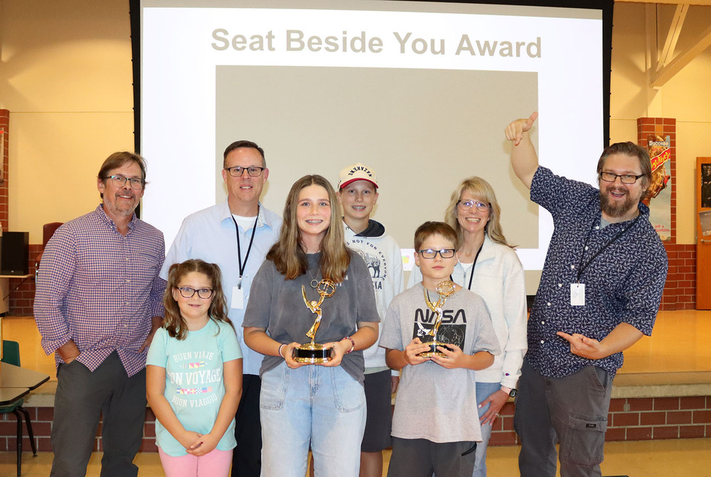 LPS filmmakers Brian Seifferlein and David Koehn stand with six members of a family at Lux Middle School. They presented former Lux student Madison with one of their Heartland Emmy Awards. Madison is holding the Emmy Award and is standing in the middle of the front row. David and Brian are smiling at the ends of the second row.