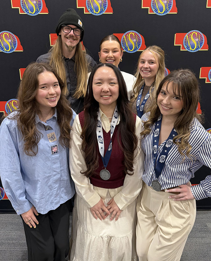 Six members of East High School's yearbook smile in two rows at the NSAA State Journalism Championships. Three of the students are wearing state medals.