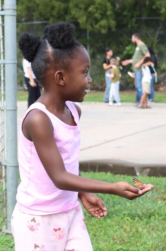 A first grade girl smiles as she holds a painted lady butterfly in her right hand at Calvert Elementary School.