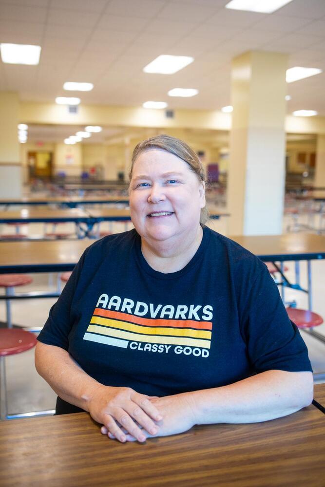 A woman sitting in a cafeteria, wearing a black shirt.