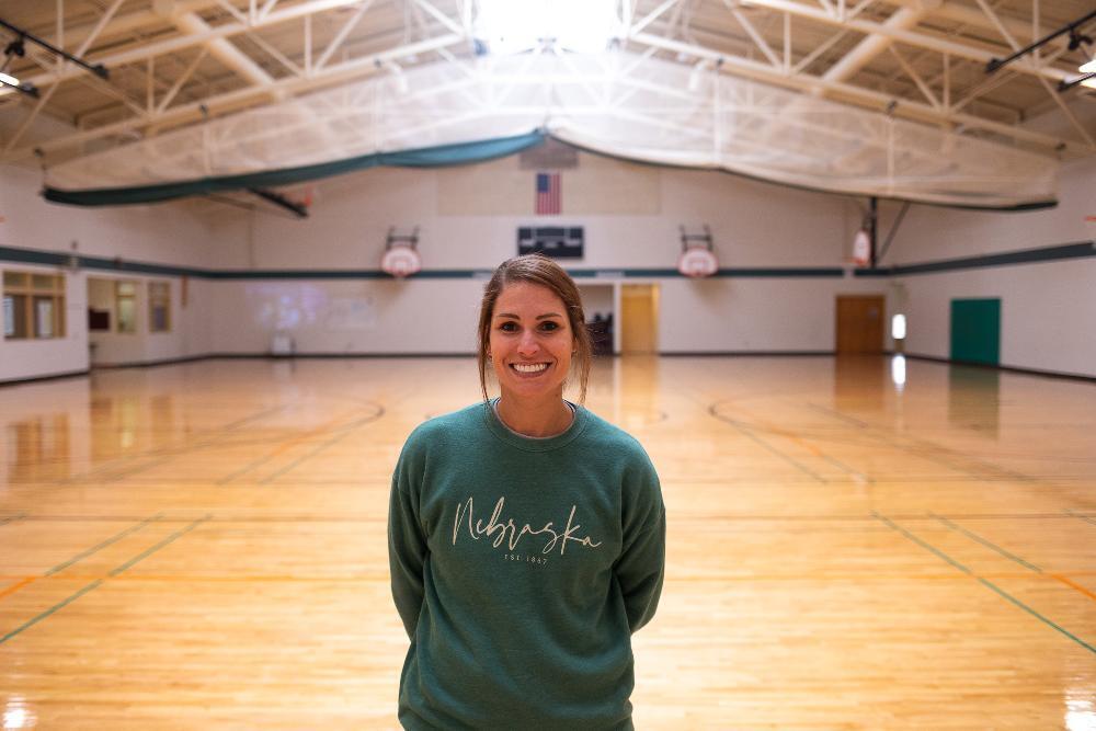 A woman standing in a gym wearing a green sweatshirt.