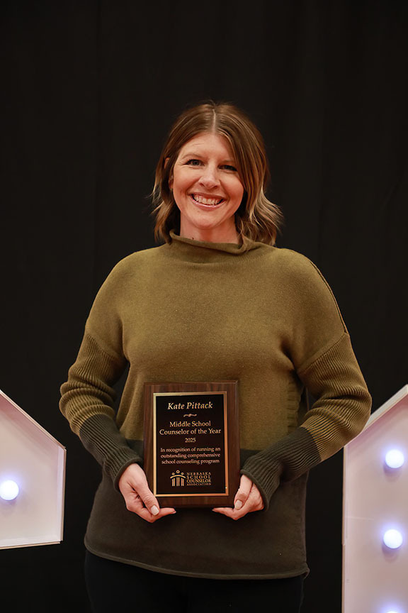 Kate Pittack smiles in front of a curtain while holding a state award with both hands. She is a school counselor at Scott Middle School.