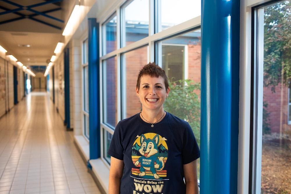 A woman standing in a school hallway wearing a navy blue t-shirt.
