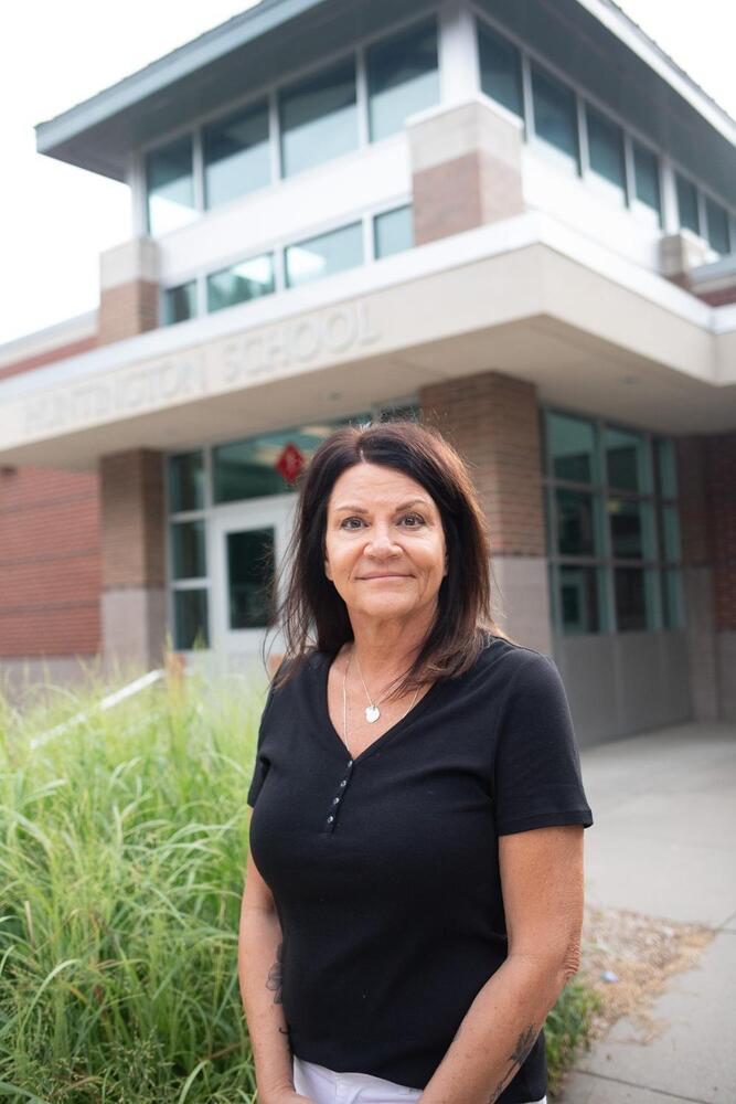 A woman standing in front of a building, wearing a black shirt.