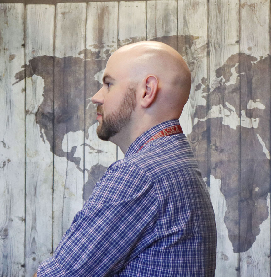 Lincoln High geography teacher Chris Turley stands in front of a wooden map of the world that is fixed to one of his classroom walls. He is facing right to left.