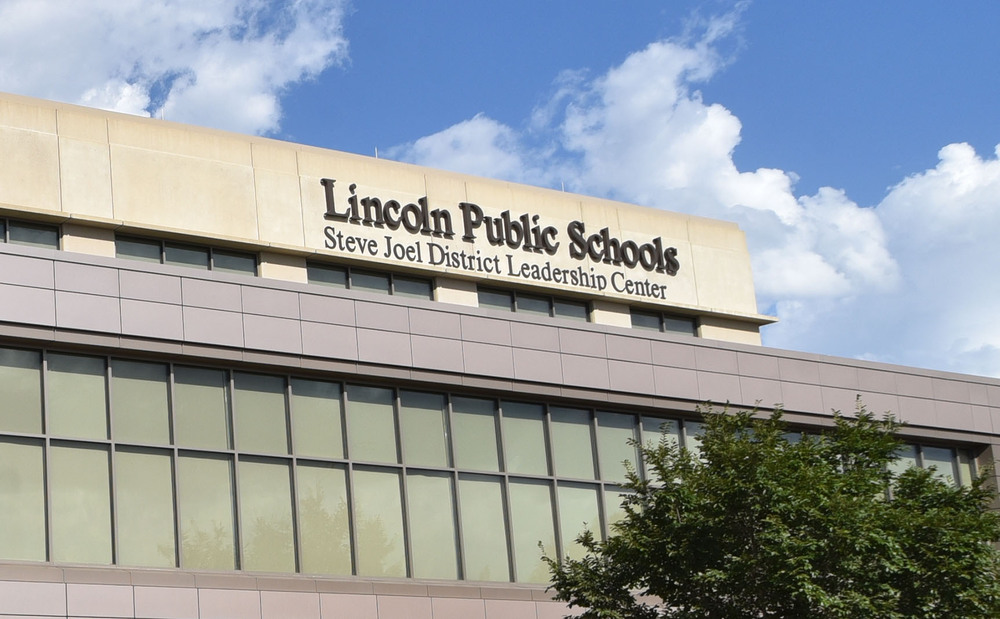 The front of the Lincoln Public Schools district office building is shown on a sunny day. There is a row of windows in the front with a tree on the righthand side.