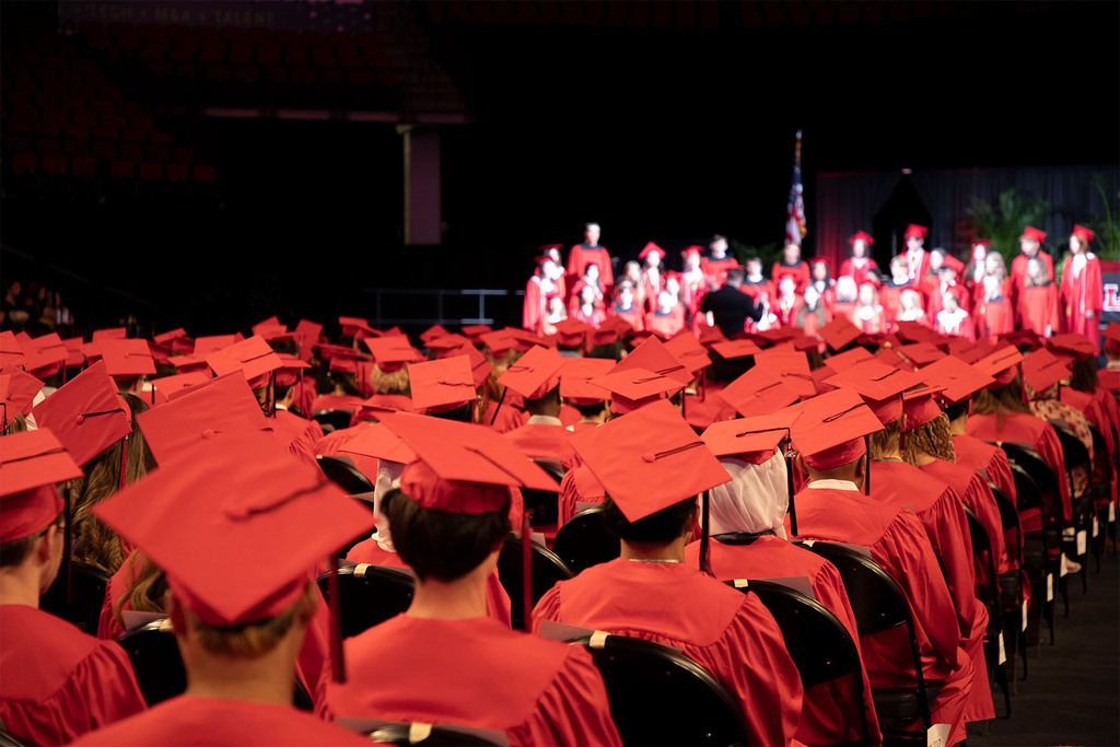 Rows of Lincoln High Graduates in red caps and gowns looking at the choir.