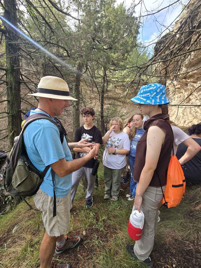 Students and professor examining item collected on hike surrounded by a rocky outcrop.