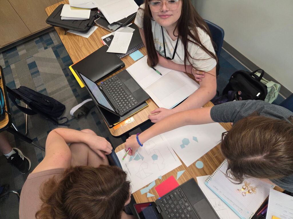 Students gathered around paper cutouts of various shapes to create composite figures.