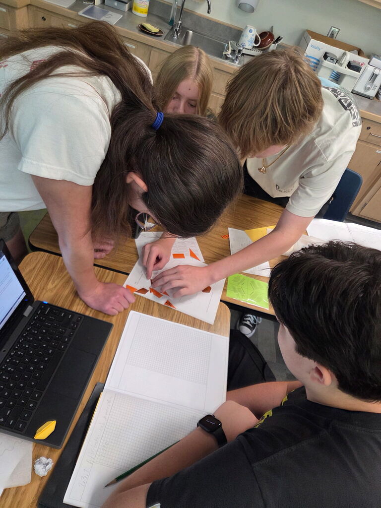 Students gathered around paper cutouts of various shapes to create composite figures.