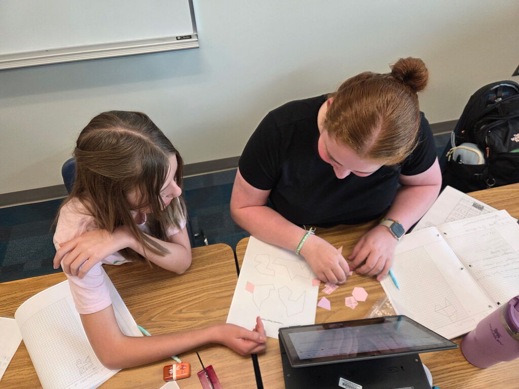 Students gathered around paper cutouts of various shapes to create composite figures.