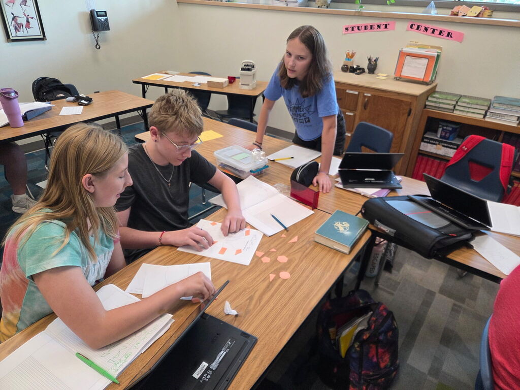 Students gathered around paper cutouts of various shapes to create composite figures.
