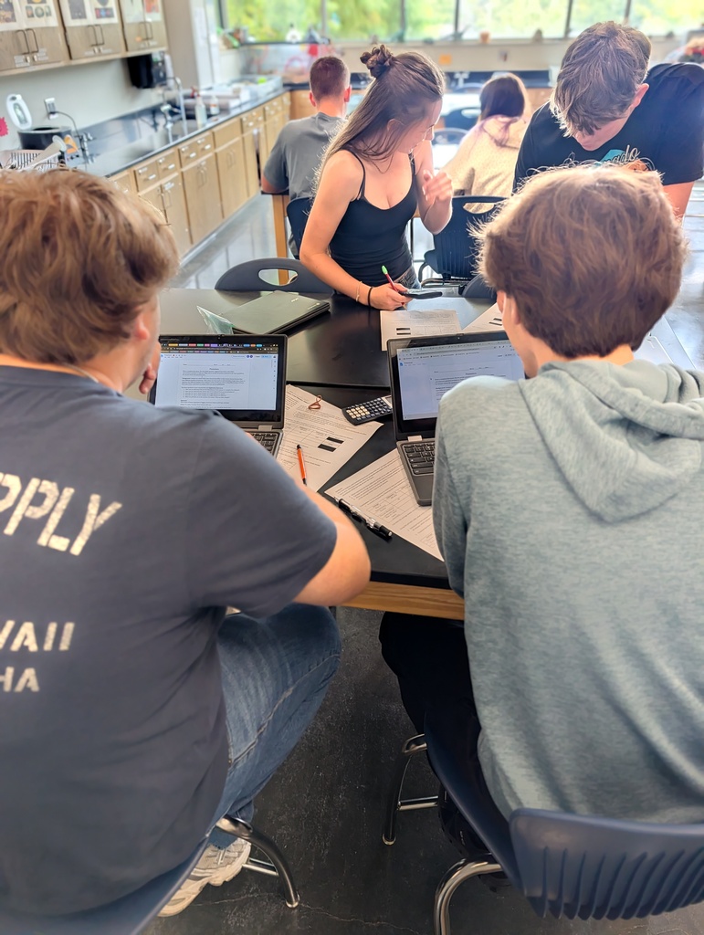 Students are collaborating on data analysis and assignment related to isotopes. Chromebooks, calculators, pencils, and lab papers on on the lab tables.