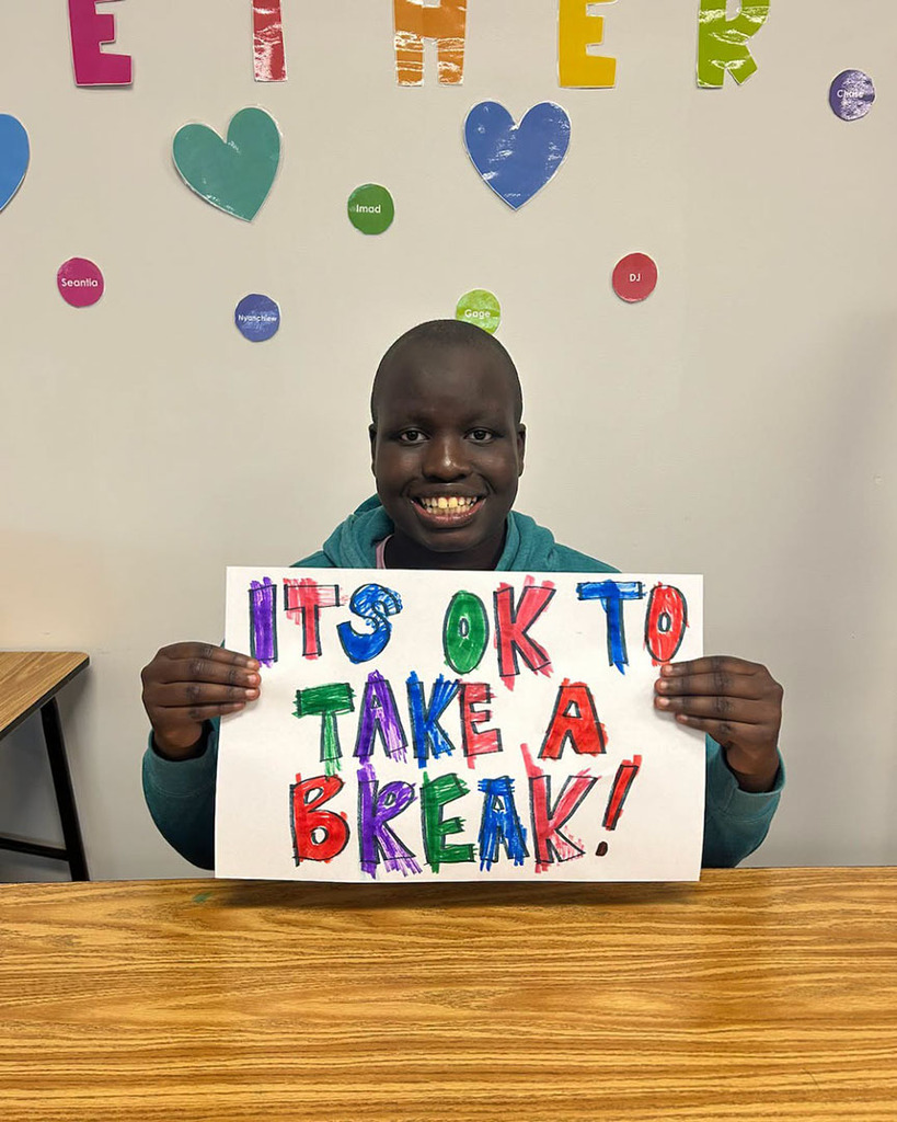 A Northwest High School student smiles as he holds a sign that says, "It's OK to take a break!"